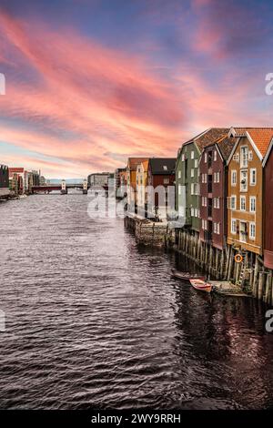 Ciel crépusculaire serein avec des teintes roses et oranges au-dessus des bâtiments historiques sur pilotis sur le front de mer de la rivière Nidelva à Trondheim, en Norvège Banque D'Images