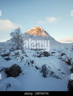 Une rivière de montagne gelée et une cascade au pied d'une montagne enneigée avec un pic ensoleillé le matin. Cascade Etive Mor. Scottish Highlands, Écosse Banque D'Images