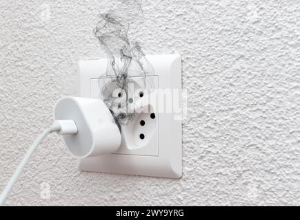 Fumée sur le chargeur de téléphone de prise de fil électrique dans l'intérieur, court-circuit électrique provoquant un incendie sur la prise de prise Banque D'Images