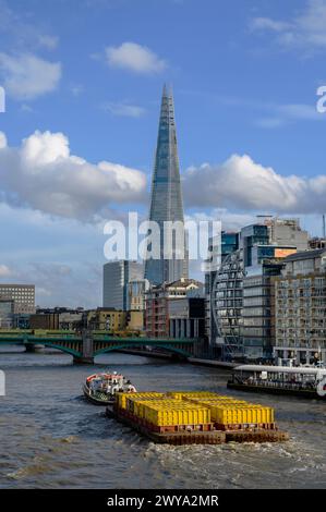 Remorqueur remorquant des conteneurs jaunes remplis de déchets compactés vers Southwark Bridge sur la Tamise à Londres, en Angleterre. Banque D'Images