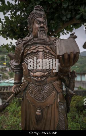 Statue en bronze minutieusement détaillée d'un guerrier chinois traditionnel en armure historique, debout sous un arbre Banque D'Images