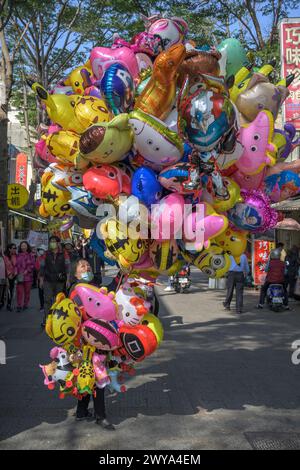 Une gamme festive de ballons colorés de personnages tenus par un vendeur dans une scène de rue animée à Lukang Banque D'Images