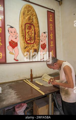 Homme âgé faisant du pain dans une petite boutique avec panneau chinois Banque D'Images