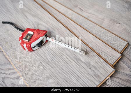 Ruban à mesurer sur des planches de parquet pour la rénovation domiciliaire, les travaux de construction et le design intérieur. Ruban à mesurer en métal sur des échantillons de panneaux stratifiés avec motif et texture en bois pour le revêtement de sol. Banque D'Images