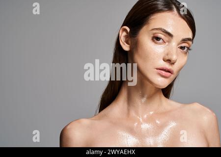 Une jeune femme caucasienne aux cheveux bruns et à la peau propre recouverte de gouttelettes d'eau, créant un effet fascinant et rafraîchissant. Banque D'Images