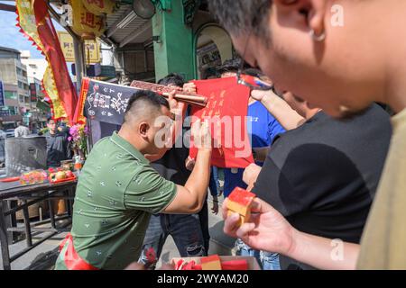 Un chaman taoïste se concentre sur l'écriture de caractères chinois pour une bénédiction sur drapeau rouge lors d'une cérémonie dans le temple Dongyue Hall Banque D'Images