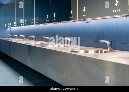 Une rangée d'éviers avec des miroirs dans une toilette publique carrelée bleue Banque D'Images