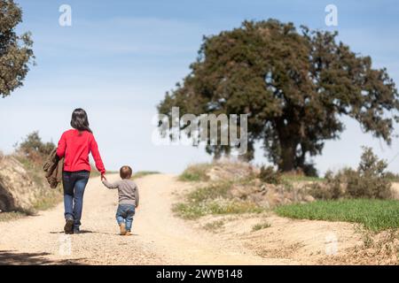 Mère et son fils de deux ans marchent le long d'un chemin vers un chêne un jour de printemps. Banque D'Images