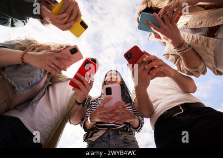 Vue à angle bas de groupe heureux méconnaissables personnes en cercle à l'aide de téléphones mobiles colorés en plein air. Banque D'Images