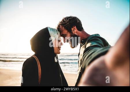 Coucher de soleil embrasser par l'océan. Un jeune couple partage un moment tendre avec pour toile de fond un coucher de soleil serein sur la plage. Banque D'Images