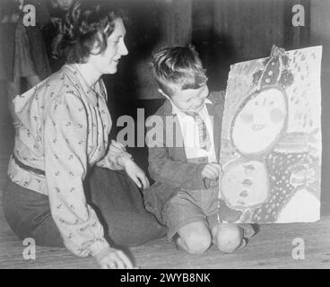 COLONIE POUR ARTISTES DE MOINS DE SIX ANS : ÉVACUÉS À DARTINGTON HALL, TOTNES, DEVON, ANGLETERRE, 1941. - Danny Ludlow, évacué de Gravesend dans le Kent, montre à son professeur Mlle Betty Hall une peinture sur laquelle il a travaillé à Dartington Hall à Totnes, Devon. Mlle Hall a été évacuée à Dartington Hall avec les enfants. , Banque D'Images