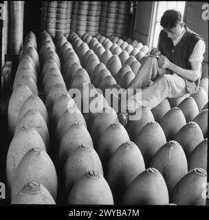 PRODUCTION DE MUNITIONS EN GRANDE-BRETAGNE, 1940 - les rangées de bombes lourdes sont vérifiées pour des numéros à une usine d'armes, quelque part en Grande-Bretagne, 1940. L'ouvrier masculin des munitions est assis au-dessus des bombes pour prendre ses notes. , Banque D'Images