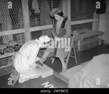 UNE VISITE ROYALE À THORP ARCH ROYAL ORDNANCE FACTORY, WETHERBY, YORKSHIRE, ANGLETERRE, ROYAUME-UNI, 1941 - sa Majesté la Reine Elizabeth est équipée de chaussures spéciales par un ouvrier de munitions avant qu'elle ne puisse entrer dans la zone «danger» de ROF Thorp Arch. La zone de l'usine où les ouvriers passent de leurs vêtements d'extérieur (le côté « sale ») à leurs vêtements d'usine et franchissent une barrière basse sur le côté « propre », usine, est connue sous le nom de « maison de transition ». Des règles strictes étaient en vigueur du côté «propre» en raison de la nature très dangereuse du travail dans les usines de remplissage. , Elizabeth, Reine Banque D'Images