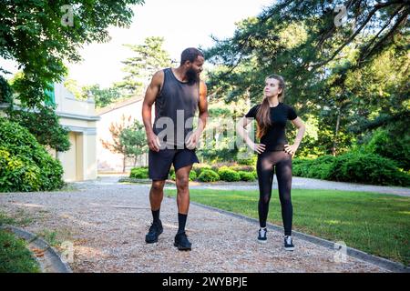 Un homme et une femme marchent sur un chemin dans un parc. L'homme porte un débardeur noir et un short, tandis que la femme porte une chemise noire et noire Banque D'Images