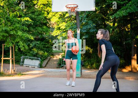 Deux femmes jouant au basket-ball dans un parc. L'un d'eux tient un basket-ball. L'autre femme porte un débardeur vert Banque D'Images