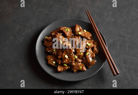 Bœuf de style asiatique avec sauce soja, oignon vert et graines de sésame sur assiette sur fond de pierre sombre. Vue rapprochée Banque D'Images