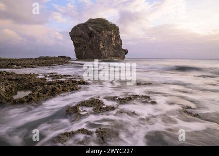 Un coucher de soleil serein avec un affleurement rocheux debout haut au milieu d'une mer soyeuse avec un effet d'exposition longue Banque D'Images