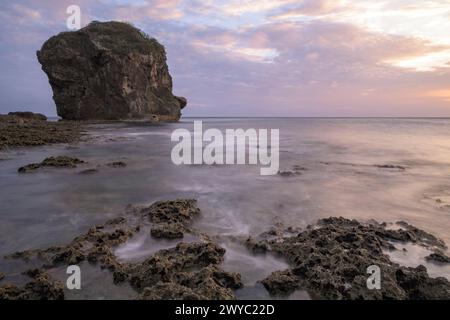 Un coucher de soleil serein avec un affleurement rocheux debout haut au milieu d'une mer soyeuse avec un effet d'exposition longue Banque D'Images