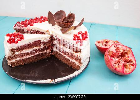 Gâteau de velours rouge aux graines de grenade, tranché sur une plaque de céramique noire, sur une table, soft focus gros plan Banque D'Images