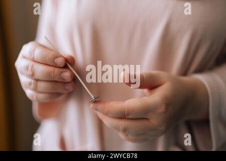 Mains rapprochées d'un artisan féminin méconnaissable tenant un outil spécial pour mélanger la cire de soja sèche pour créer un mélange de construction de bougie. Banque D'Images