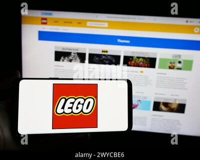 Personne tenant un smartphone avec le logo de la société danoise de jouets de construction LEGO COMME en face du site Web. Concentrez-vous sur l'affichage du téléphone. Banque D'Images