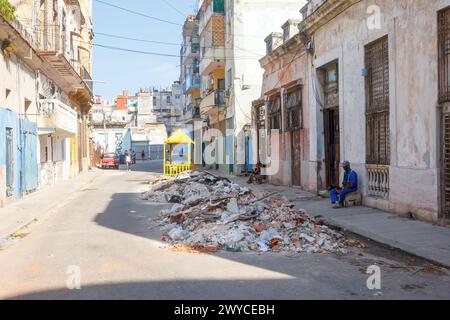 Homme cubain assis sur le trottoir, tas de gravats dans la rue de la ville à la Havane, Cuba Banque D'Images