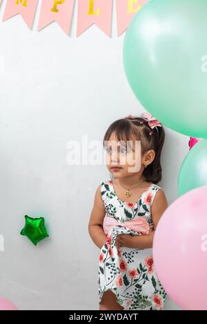 petite brune latina girl serrant sa robe de fleur, entourée de ballons Banque D'Images