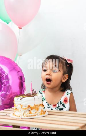 petite fille brune latine ouvrant sa bouche pour souffler la flamme des bougies sur son gâteau d'anniversaire Banque D'Images