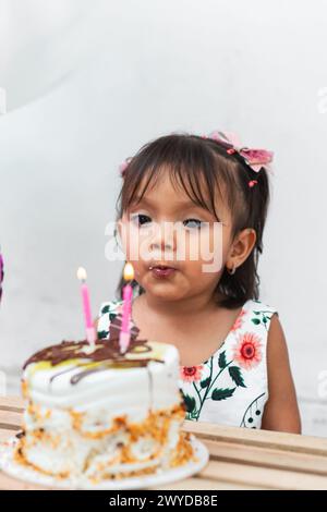 petite fille de brune de latina essayant de souffler les bougies qui sont sur son gâteau d'anniversaire Banque D'Images