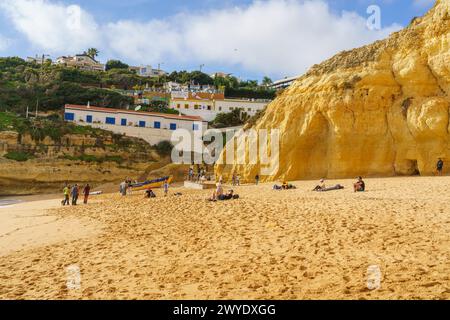 Les visiteurs profitent d'une journée à la plage sous les maisons à flanc de falaise de l'Algarve. Banque D'Images