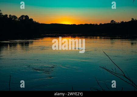 Great Don River dans le milieu. Le coucher de soleil orange se reflète dans l'eau. Silhouette noire de forêt côtière. Il y a beaucoup de trichoptères volant au-dessus de s. Banque D'Images