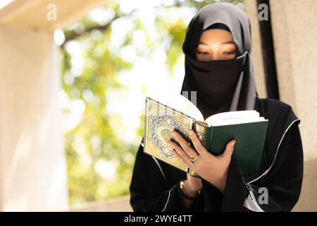 Femme musulmane niqab lisant et apprenant le Coran et la foi le livre du Saint Al Coran. Arabe saoudienne noire chador dame. Banque D'Images