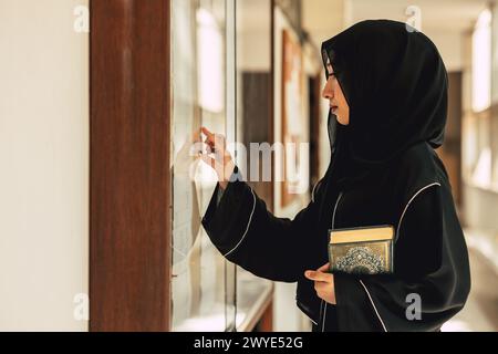 Femme musulmane niqab lisant et apprenant le Coran et la foi le livre du Saint Al Coran. Arabe saoudienne noire chador dame. Banque D'Images