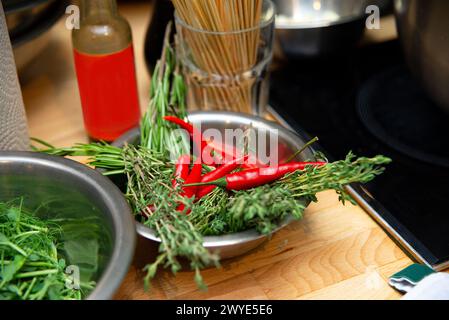 La cuisine du chef comprend un bol d'herbes fraîches et de piments rouges, avec des ustensiles de cuisine en arrière-plan. Banque D'Images