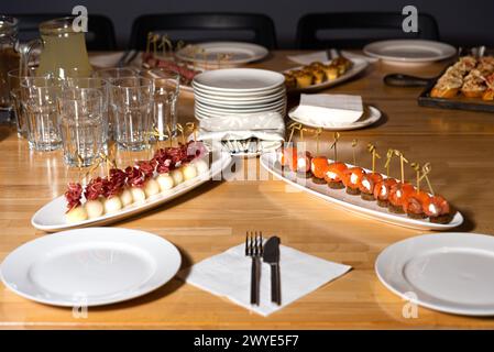 Une table de banquet élégamment décorée avec un assortiment de canapés gastronomiques, verres et assiettes, prête pour un événement traiteur. Banque D'Images