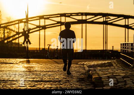 06 avril 2024, Hesse, Francfort/main : un homme fait du jogging au lever du soleil dans l'Osthafen. Les températures dans la métropole Rhin-main devraient atteindre 25 degrés au cours de la journée. Photo : Andreas Arnold/dpa Banque D'Images