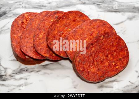 Nduja de porc et piment calabrique, tranches de saucisse épicées sur plateau en marbre blanc. Chemin de détourage inclus Banque D'Images