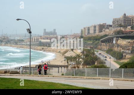 Tarragone, Espagne - 6 avril 2024 : scène côtière de Tarragone avec des gens appréciant la plage et l'architecture urbaine en arrière-plan, capturant l'essen Banque D'Images