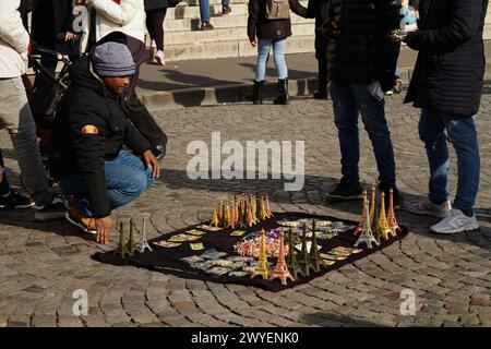 Vendeur de rue avec tours Eiffel miniatures et cadenas étalés sur Une feuille à vendre sur les pavés devant le Sacré-coeur, Paris, France Banque D'Images