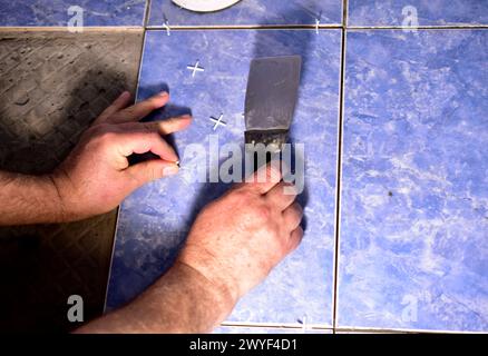 Gros plan des mains de l'homme, dans l'une desquelles il voit une spatule, et l'autre repose sur une tuile. Banque D'Images