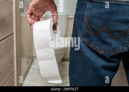 La main d'un homme plus âgé tenant un rouleau de papier toilette devant les toilettes. Banque D'Images