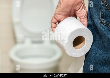 La main d'un homme plus âgé tenant un rouleau de papier toilette devant les toilettes. Banque D'Images