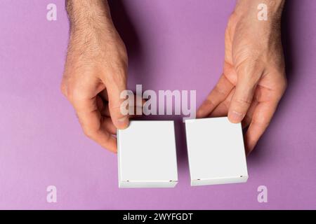Main masculine tenant deux boîtes de pilules pour l'appariement devant un fond violet, chemin de sélection inclus. Banque D'Images
