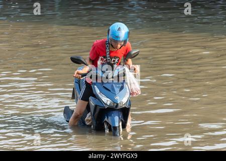 SAMUT PRAKAN, THAÏLANDE, 11 février 2024, Un homme pousse une moto dans une rue inondée, Thaïlande Banque D'Images
