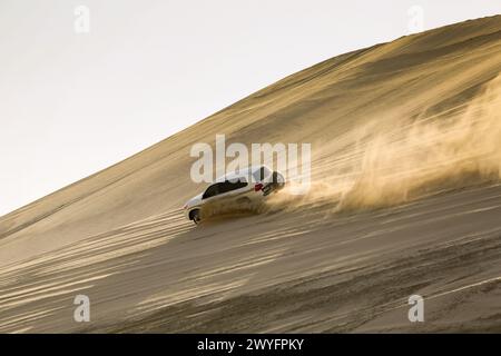 La balade en 4 roues motrices au désert arabe au-dessus des dunes. Une chaude journée dans le désert. Voiture SUV blanche conduisant sur une dune de sable près du Qatar, Banque D'Images