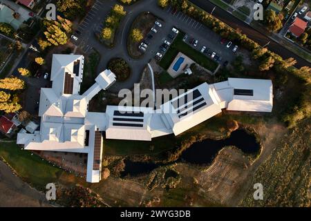 Un hôtel écologique au toit blanc avec lac, piscine et parking, aérien en bas. Banque D'Images