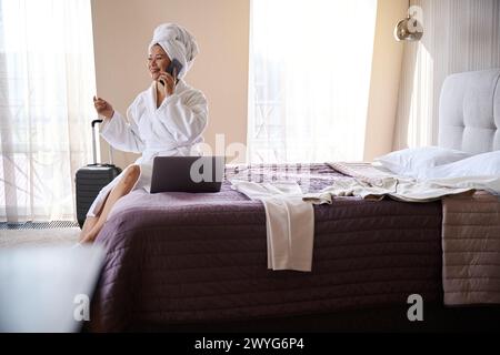 Femme d'affaires joyeuse ayant une conversation sur smartphone dans sa chambre d'hôtel Banque D'Images