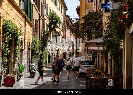 Rome, Italie - 14 août 2023 : une ruelle avec assis en plein air et touristes marchant. Immeubles d'appartements avec plantes et volets aux fenêtres Banque D'Images