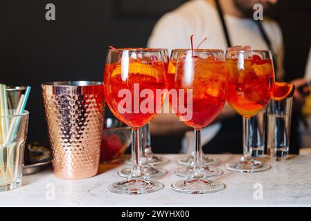 Apéritif rafraîchissant cocktails Spritz avec glace et tranches d'orange, servi dans des verres à vin sur un comptoir de bar en marbre, avec un barman en arrière-plan. Banque D'Images