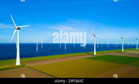 Une scène étonnante se déroule comme un groupe de moulins à vent debout dans un champ à côté de l'océan dans le Flevoland néerlandais pendant la saison vibrante du printemps. jour de la terre, écologique, énergie verte Banque D'Images